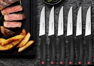 six steak knives laying on a table with a tray of food