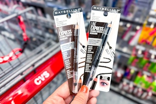hand holding two maybelline line express eyeliner next to cvs shopping cart