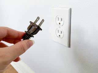 A person's hand holding a plug near an outlet that they just unplugged it from.