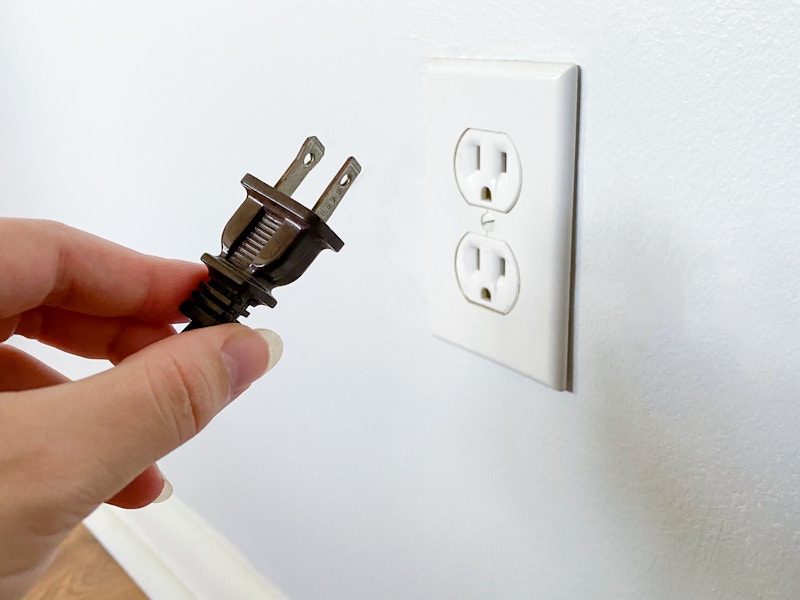 A person's hand holding a plug near an outlet that they just unplugged it from.