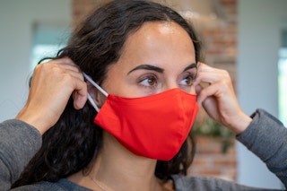 A woman putting on a fabric face mask.