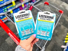 person holding 2 packages of listerine pocketpacks over a cart