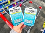 person holding 2 packages of listerine pocketpacks over a cart