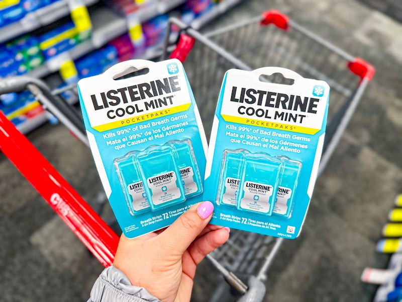 person holding 2 packages of listerine pocketpacks over a cart