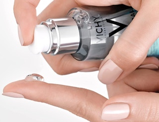 blue bottle of face serum squeezing product in hand