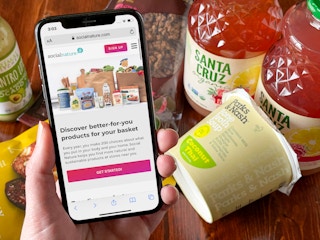 A cell phone with the Social Nature website pulled up on the screen next to a bunch of organic products