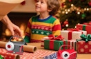 an adult and kid next to wrapping paper and cutters on a table