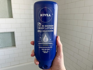 A person holding a bottle of Nivea in shower body lotion in front of a shower.