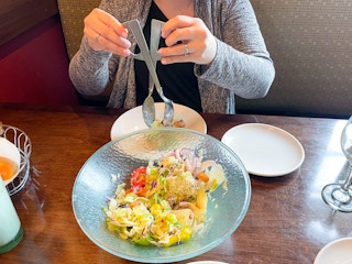 A person using the salad tongs to grab some salad out of the large Olive Garden salad serving bowl.