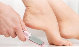 a hand holding an electric foot callus remover next to their foot