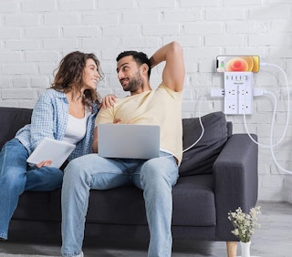 a couple on a couch with their laptop plugged into the wall