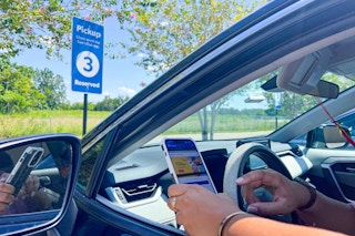 a person sitting in a car looking at their phone while in sam's club curbside pick up area 