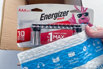 a hand holding a battery above a box of batteries