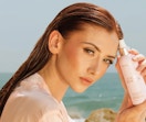 a woman holding a bottle of hair detangling spray on a beach
