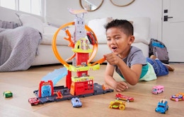 a kid on the floor playing with a Hot Wheels playset