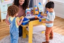 Lifestyle image of the KidKraft play kitchen being used by 2 children and mother figure