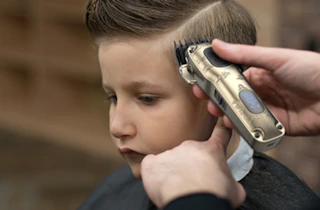 a person cutting a kid's hair with hair clippers