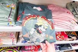 person grabbing a mickey mouse graphic tee from a shelf of graphic tees