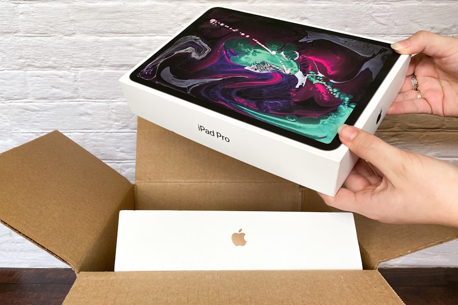 A person taking an iPad pro out of a shipping box with another Apple product inside.