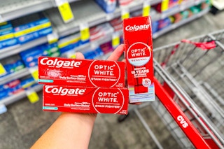 person holding 3 colgate optic white toothpastes over a cvs cart