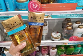 a hand holding two two bottles of hair oil in a box
