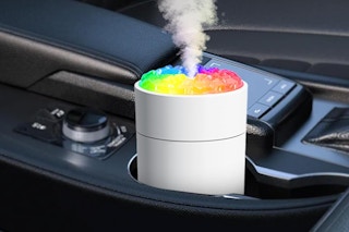 In a car cup holder sits a white mini diffuser (humidifier?) with rainbow colors on top