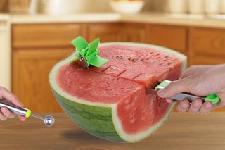 People cutting a watermelon on kitchen counter