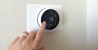 person's hand adjusting a google nest thermostat indoors