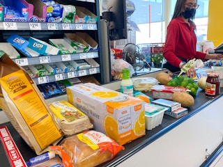 A checkout lane conveyer belt filled with grocery items and a cashier scanning them.