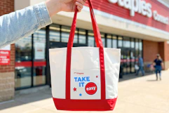 hand holding a staples tote bag in front of a staples store
