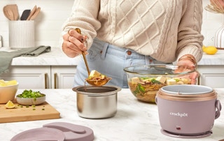 a person putting food in an electric lunch box on a kitchen counter