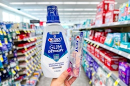 person holding crest mouthwash and toothpaste in an aisle