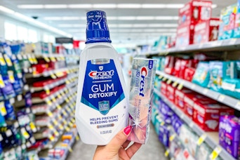 person holding crest mouthwash and toothpaste in an aisle