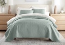 A sage colored Linens & Hutch quilt set in a bedroom. 