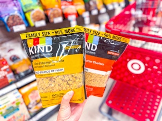 hand holding 2 kind family size granola bags in front of a parked cart