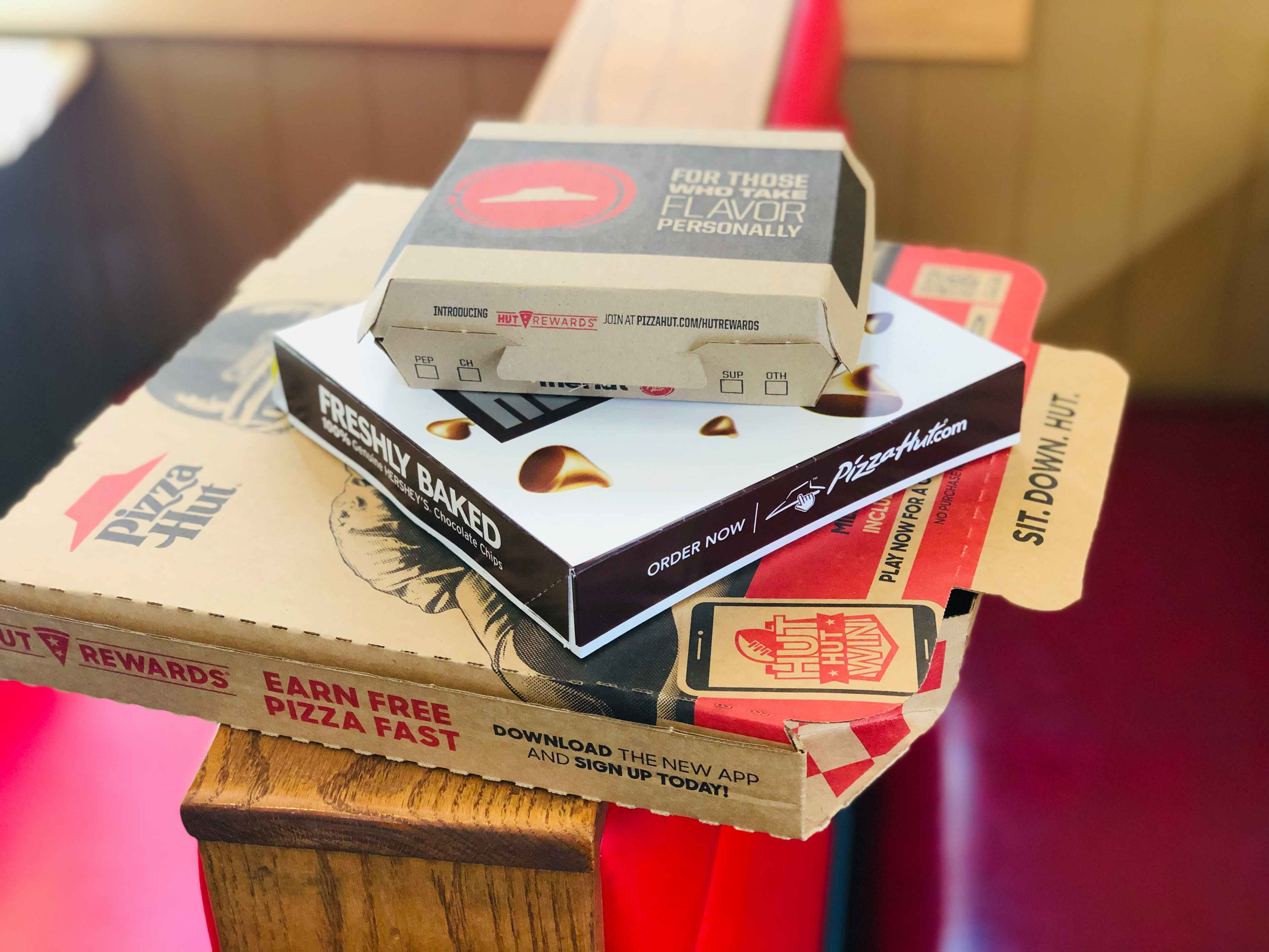 A pizza box, wing box, and dessert box from Pizza Hut stacked on top of each other