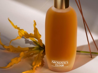 an orange and gold bottle next to a leaf and incenses 