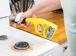 a person spraying a stove with a cleaner in a yellow bottle