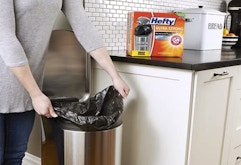 Person putting trash bags into a trash can.