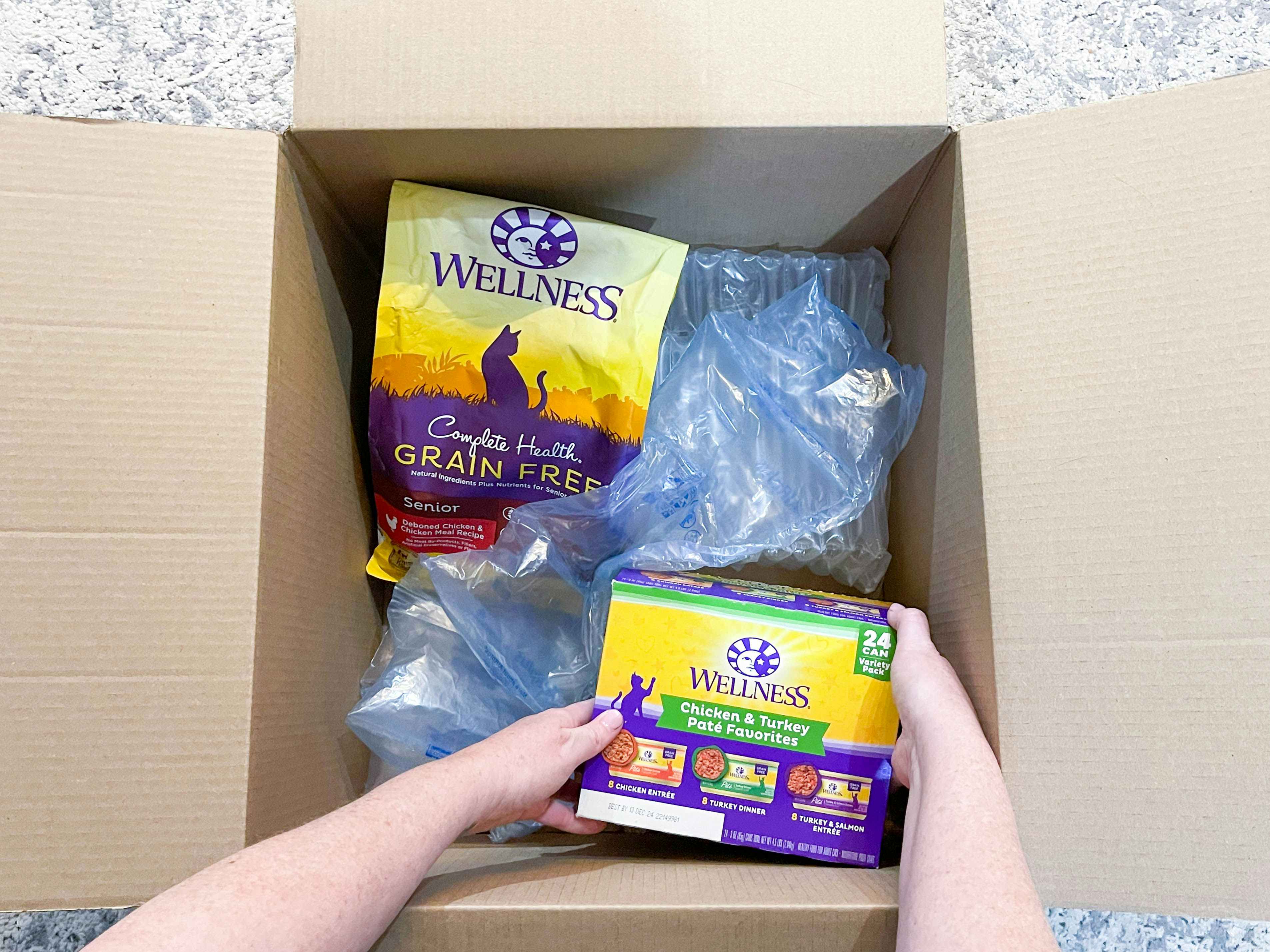 a person taking a box of cat food out of a delivery box