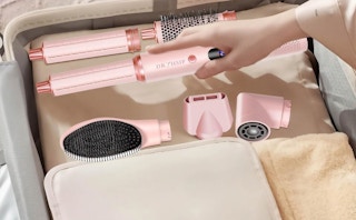 a hand putting a pink air hair styler in a suitcase