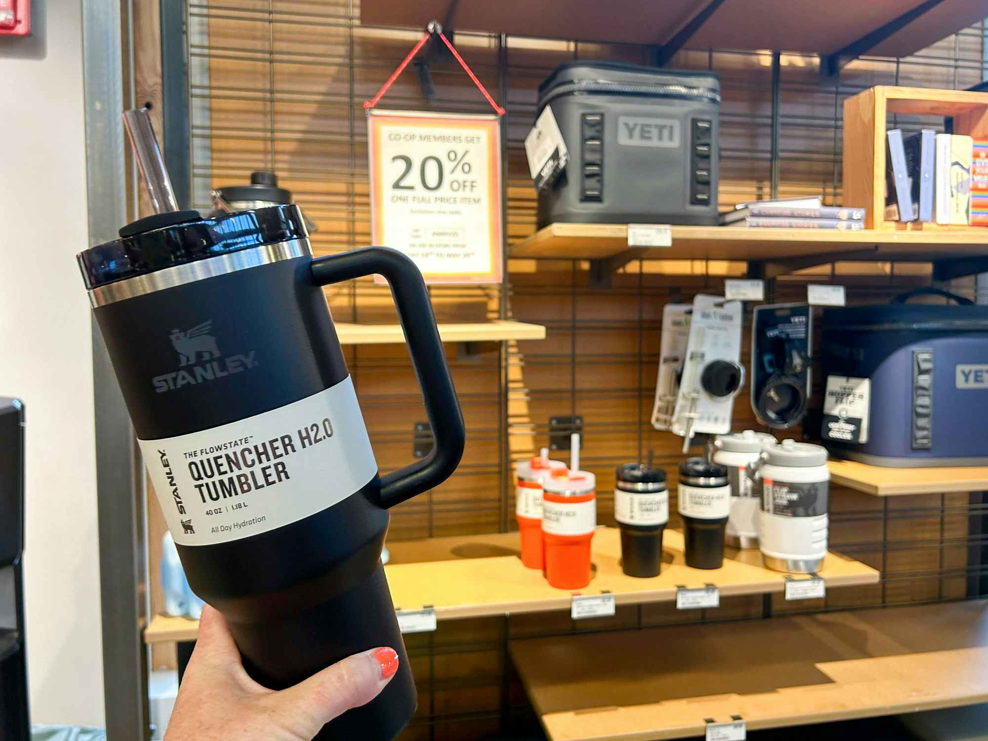 Someone holding a Stanley tumbler in front of a 20% off sign in REI