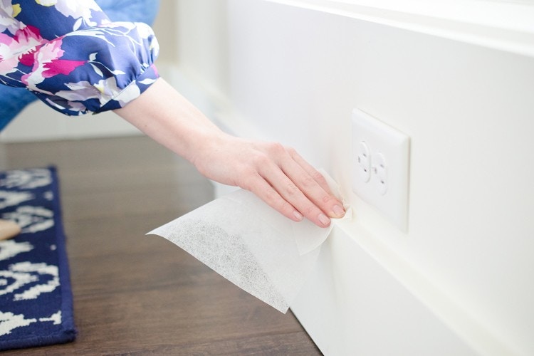 Person cleaning baseboards with dryer sheets