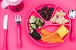Lifestyle image of the green sprouts learning dining plate in the color pink with various food groups