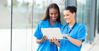 two medical professionals in scrubs smiling and looking at laptop