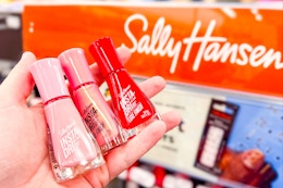 person holding 3 sally hansen nail polishes by the display
