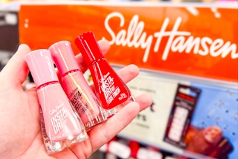 person holding 3 sally hansen nail polishes by the display