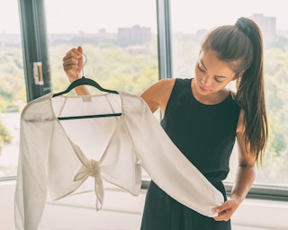 woman holding up crop top on hanger in her apartment