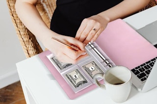 a person at a desk with a pink binder with money and a laptop