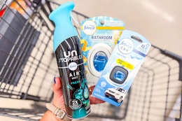 person holding febreze air freshener, small spaces, and car vent clip over a cart